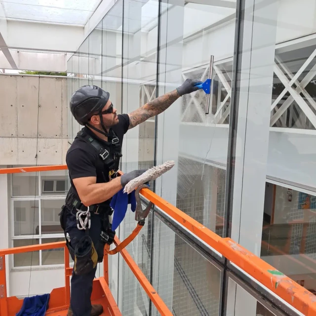 Profissional utilizando rapel limpando uma fachada de vidro moderna
